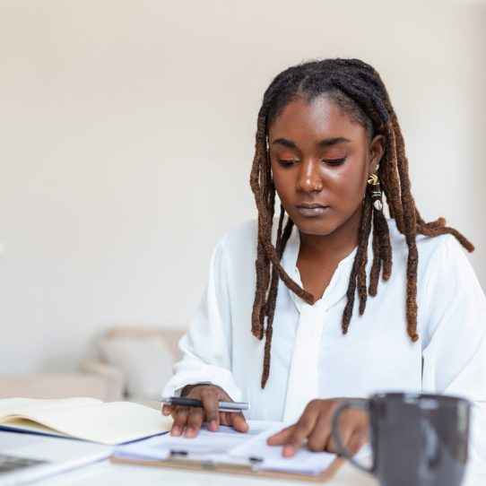 Remote job, technology and people concept - happy smiling young black business woman with laptop computer and papers working at home office